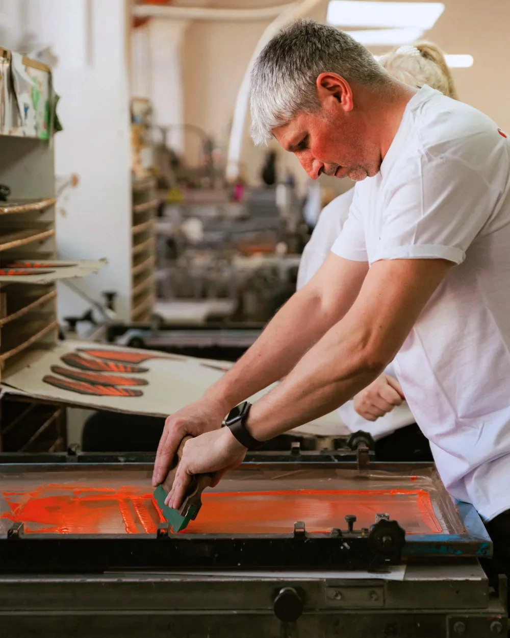 Operator trăgând cerneală portocalie pe ecran de serigrafie - Antel Print