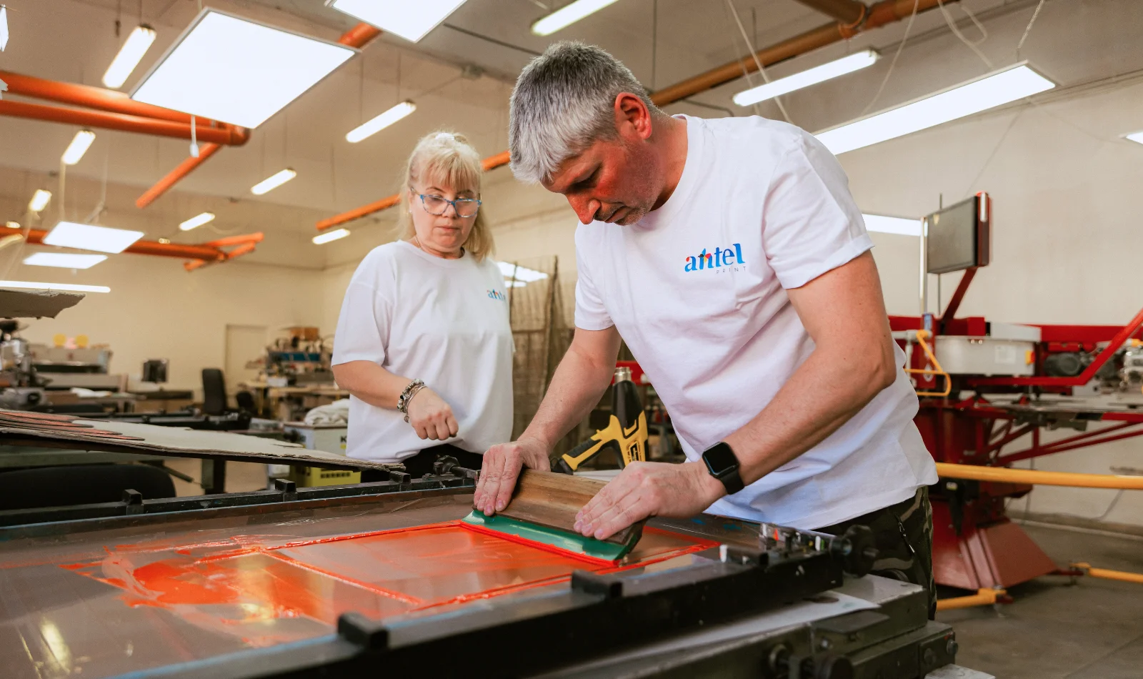 Operatori Antel Print trăgând cerneală portocalie pe ecran de serigrafie - Antel Print